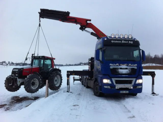 Lastbil med kran som lyfter en traktor
